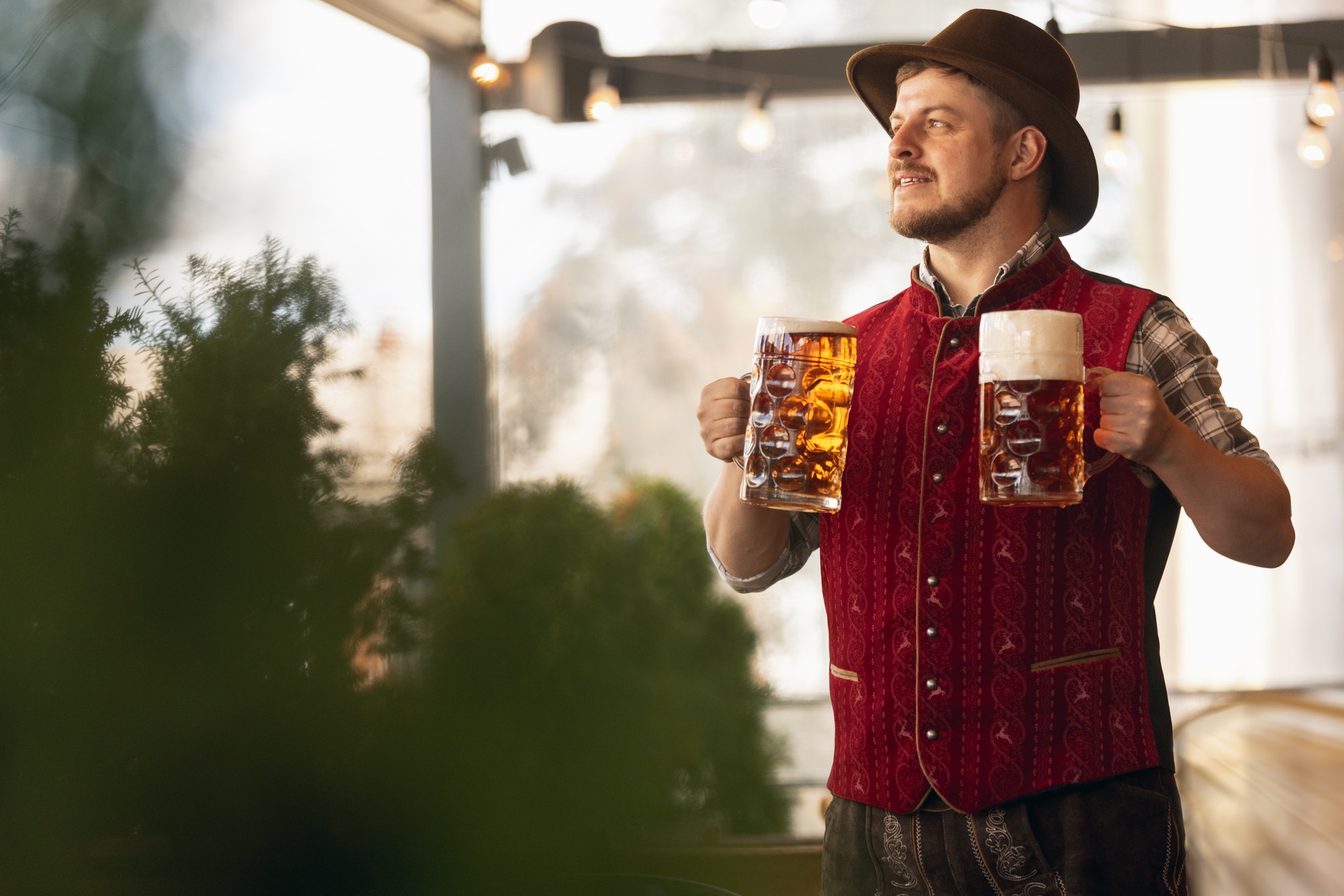 Happy smiling man, waiter in traditional Austrian or Bavarian costume holding mug, glass of dark
