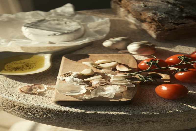 A rustic wooden table with a woven basket full of freshly picked porcini and wild herbs, with a farmhouse in the background