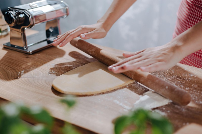 Hands of an elderly Italian woman rolling fresh pasta dough on a floured wooden board