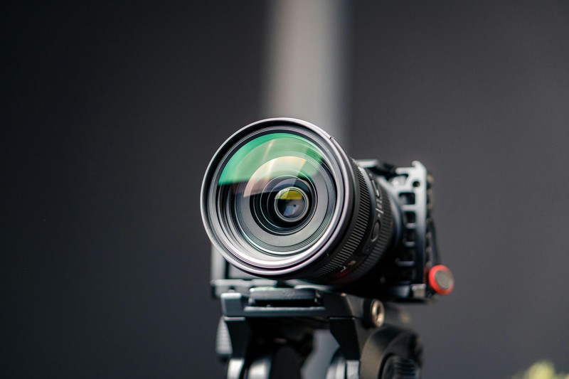 Photography gear including a tripod, camera lens, and filters set up on a stone wall overlooking an Italian valley