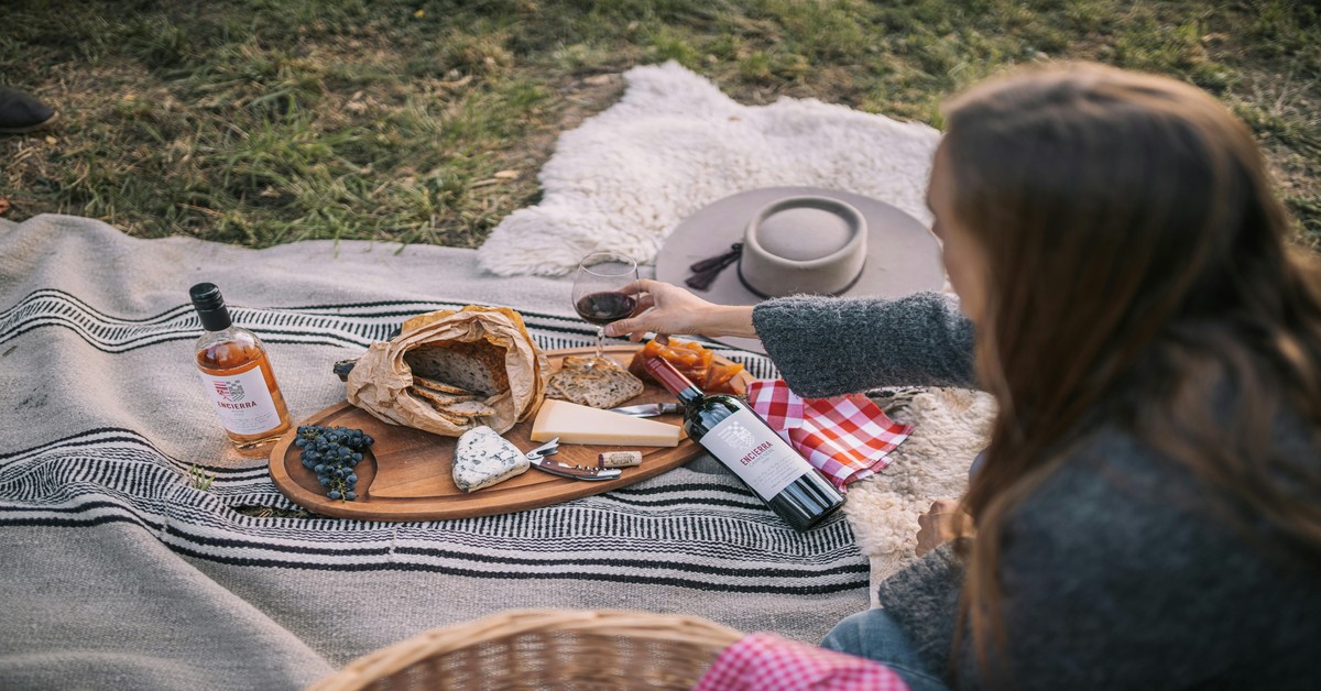 A romantic picnic blanket spread between rows of grapevines in a Tuscan vineyard with bread and a bottle of wine